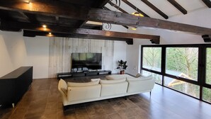 Un salón amplio con una televisión de pantalla plana grande, un sofá de cuero blanco y una chimenea de piedra.