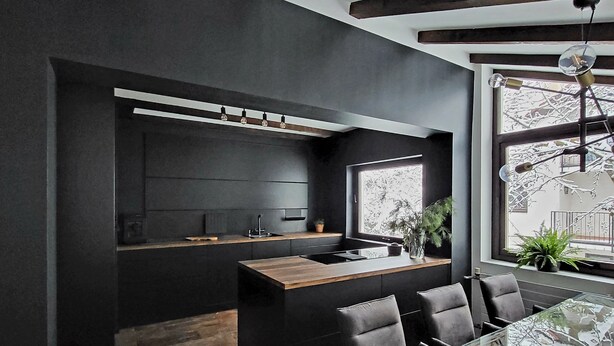 Una cocina moderna con paredes oscuras, una isla de madera y una mesa de comedor de vidrio con sillas.