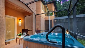 Un bain à remous doté d’un robinet noir, entouré d’une terrasse en bois et de chaises, avec une porte en verre et un luminaire fixé au mur.