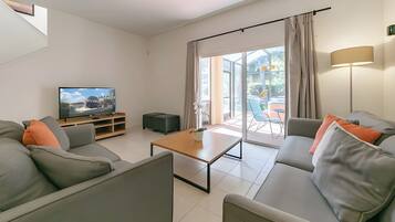 Una sala de estar moderna con un televisor de pantalla plana, sofás grises, una mesa de centro de madera y un ventanal corredizo que da a un espacio exterior.