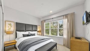 A modern bedroom with a large bed, bedside tables, a bench, a TV, and a window with curtains.
