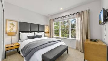 A modern bedroom with a large bed, bedside tables, a bench, a TV, and a window with curtains.