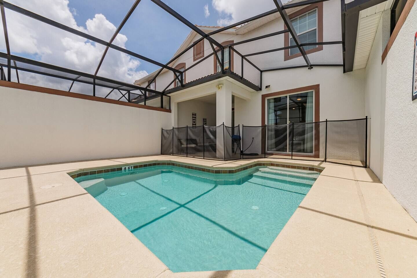 A swimming pool with a glass enclosure, a covered patio area, and a view of a residential building.