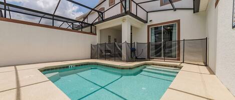 A swimming pool with a glass enclosure, a covered patio area, and a view of a residential building.