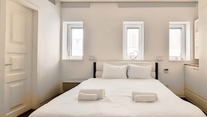 Une chambre d’hôtel avec un grand lit, deux fenêtres, une armoire et une table de chevet.