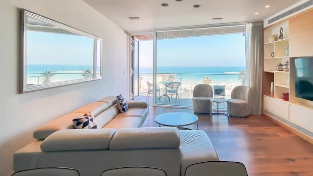 Un salon moderne avec un canapé, un téléviseur et un balcon offrant une vue sur la mer.