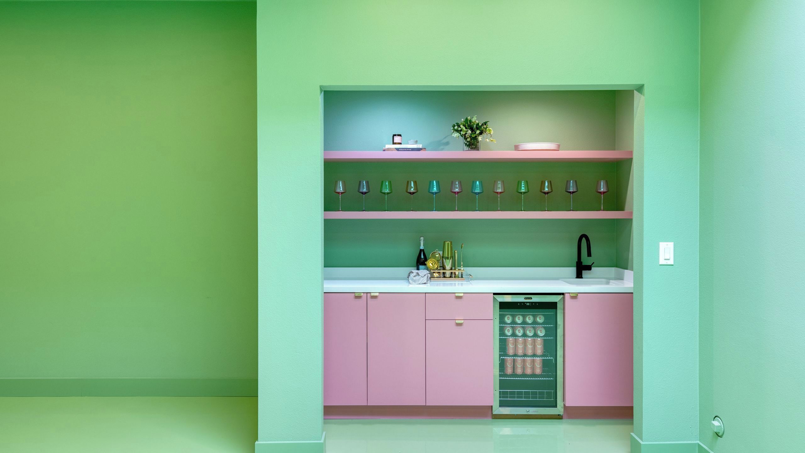 Eine Küche mit rosa Arbeitsplatte, Spüle und Weinkühlschrank mit bunten Gläsern.