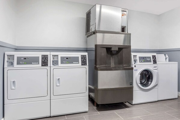 A laundry room with two front-loading washers and a tall stainless steel dryer. - Suburban Studios Gainesville (Gainesville)