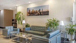 Un vestíbulo moderno con un sofá verde, sillones azules, una mesa de centro de vidrio y plantas en macetas.