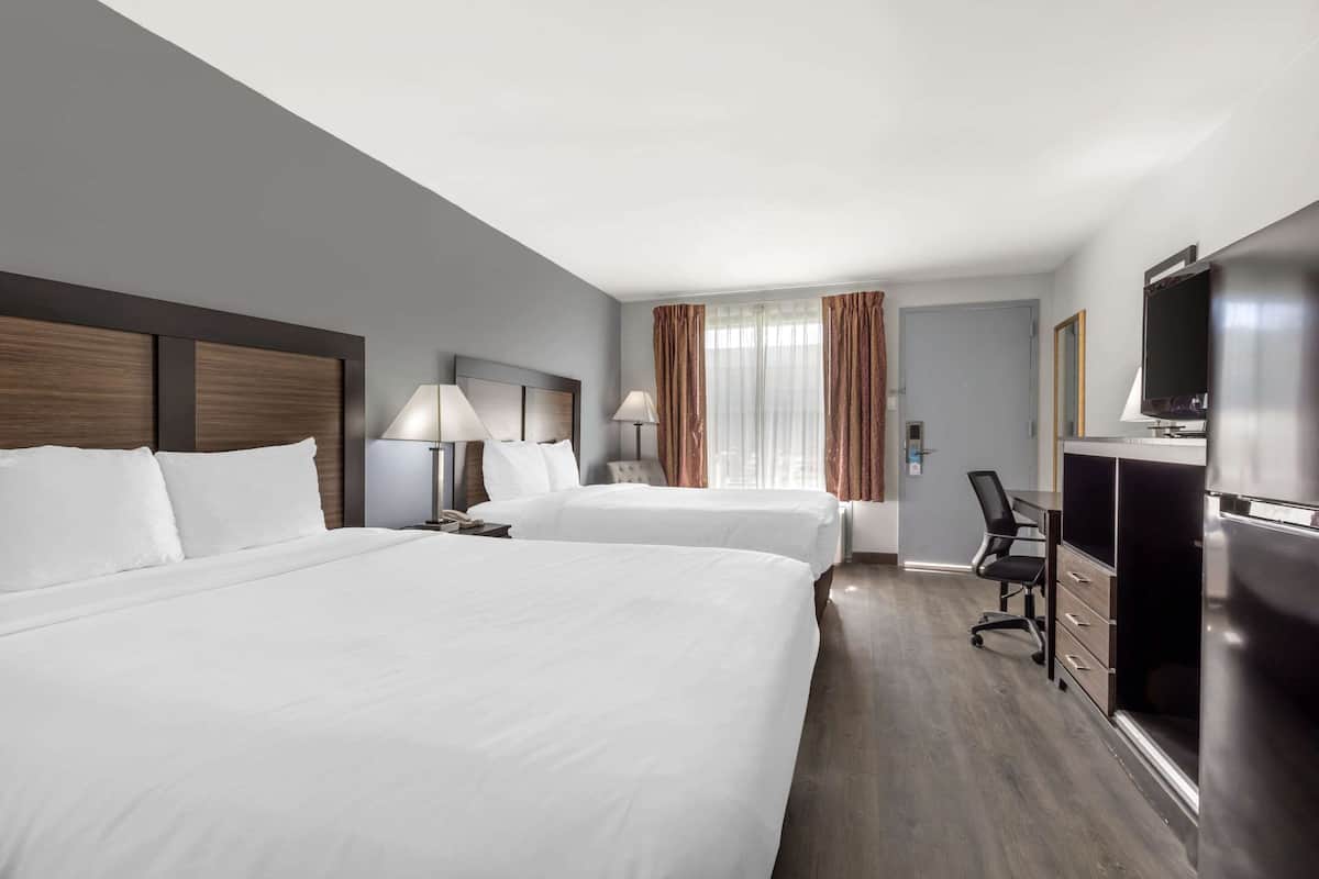 A hotel room with two beds, a desk with a chair, a television, and a minibar.