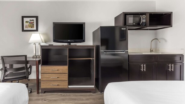 Habitación de hotel con cama, escritorio con computadora, televisor, microondas y refrigerador.