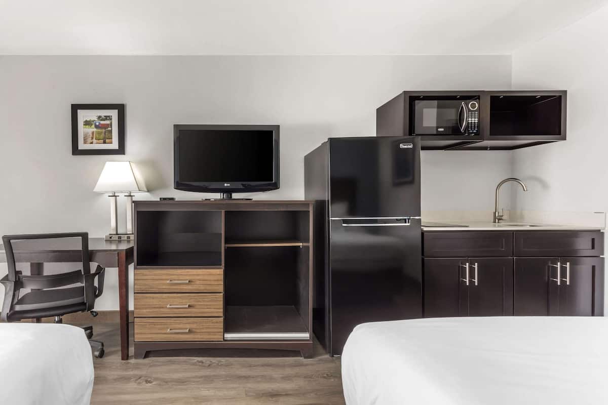 A hotel room with a bed, a desk with a computer, a TV, a microwave, and a refrigerator.
