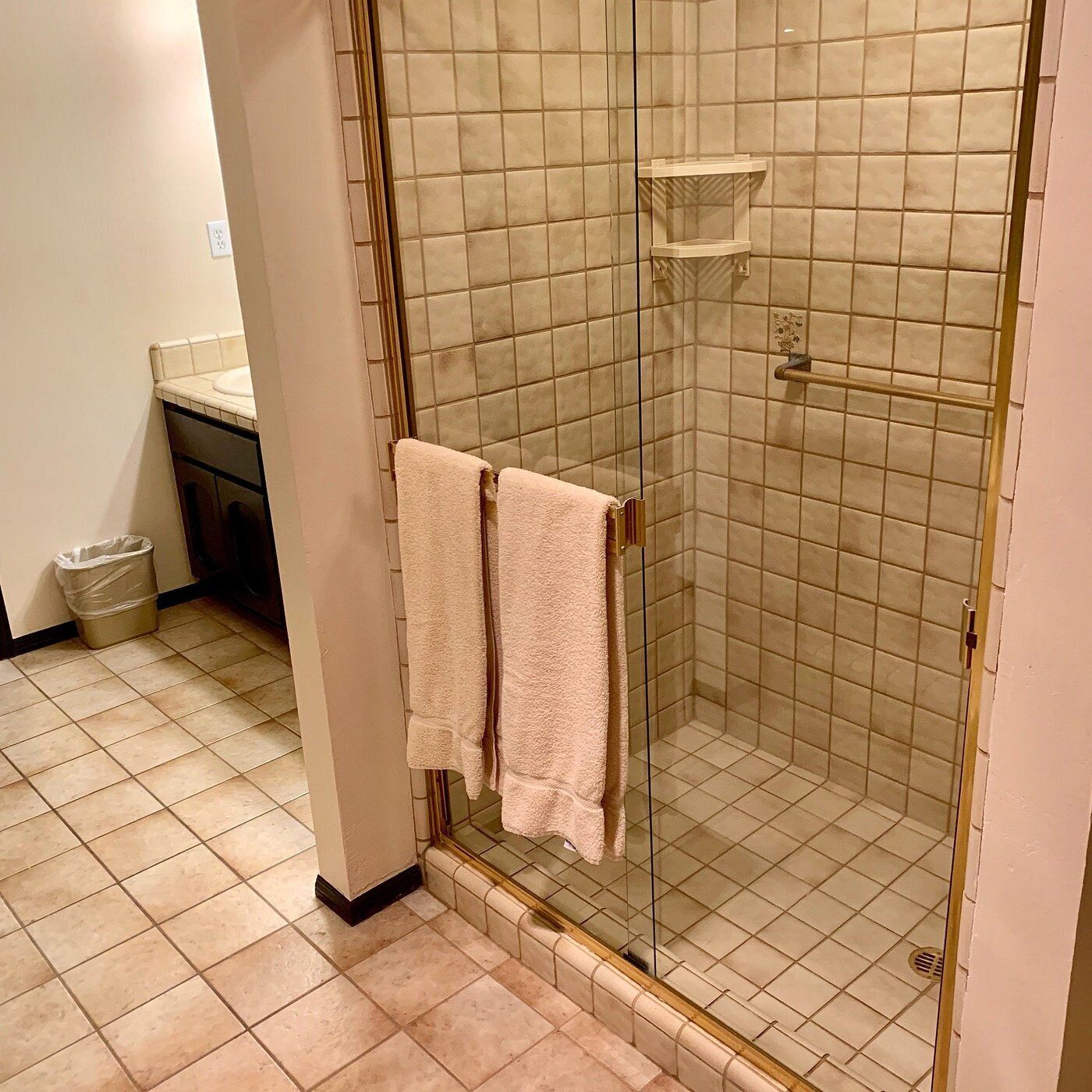 A bathroom with a glass-enclosed shower, tiled walls, and a trash bin.