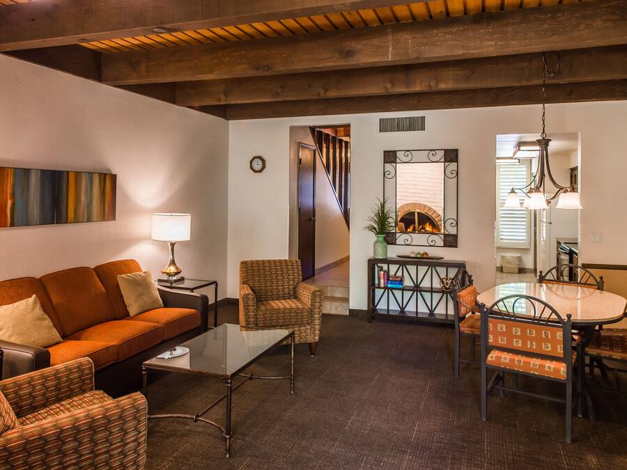 Una sala de estar con un sofá, sillones, una mesa baja, una mesa de comedor con sillas, una chimenea y una escalera que sube a otro nivel.