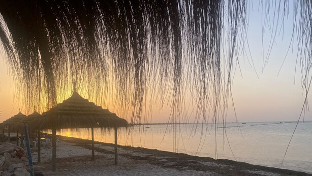 A beach with a thatched-roof structure and rocks in the foreground.