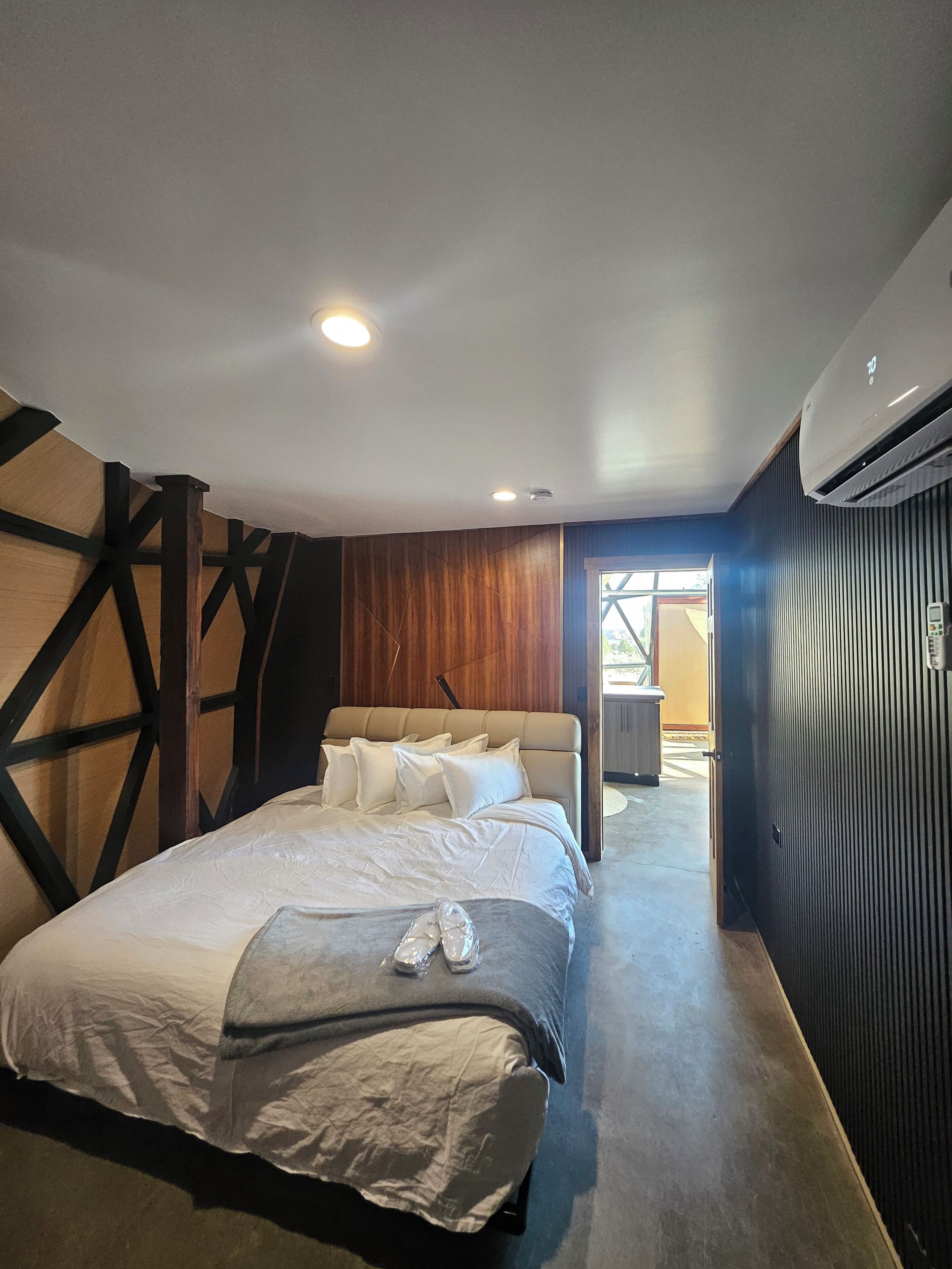 A modern bedroom with a large bed, wooden paneling, and an air conditioning unit.