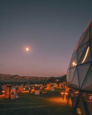A modern building with a unique geometric design, surrounded by outdoor seating areas and a view of the landscape.