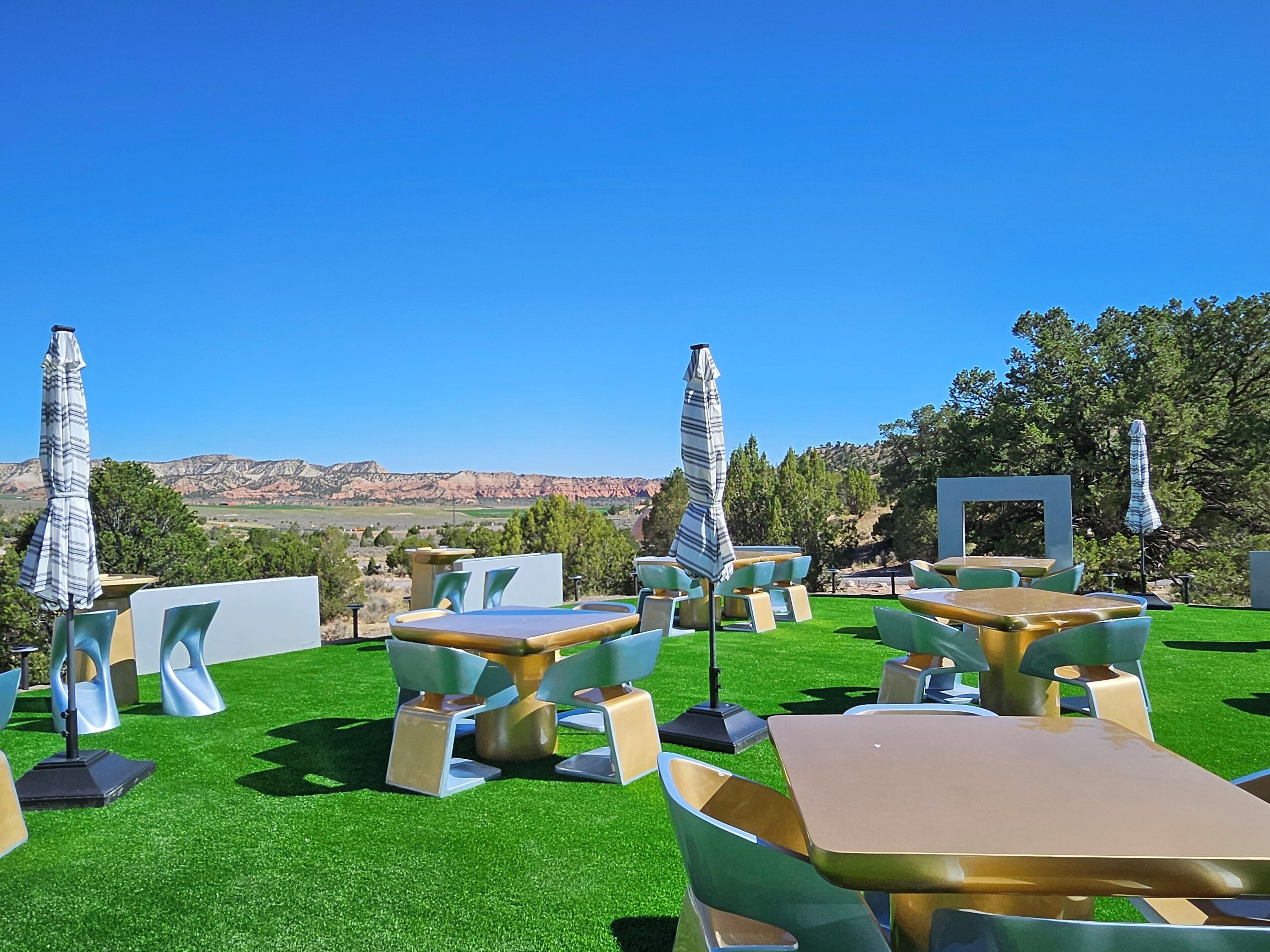 An outdoor seating area with tables and chairs, surrounded by a well-maintained lawn, with a scenic mountain view in the background.