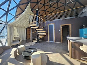 A spacious room with a large window, a spiral staircase, and a seating area with a coffee machine.