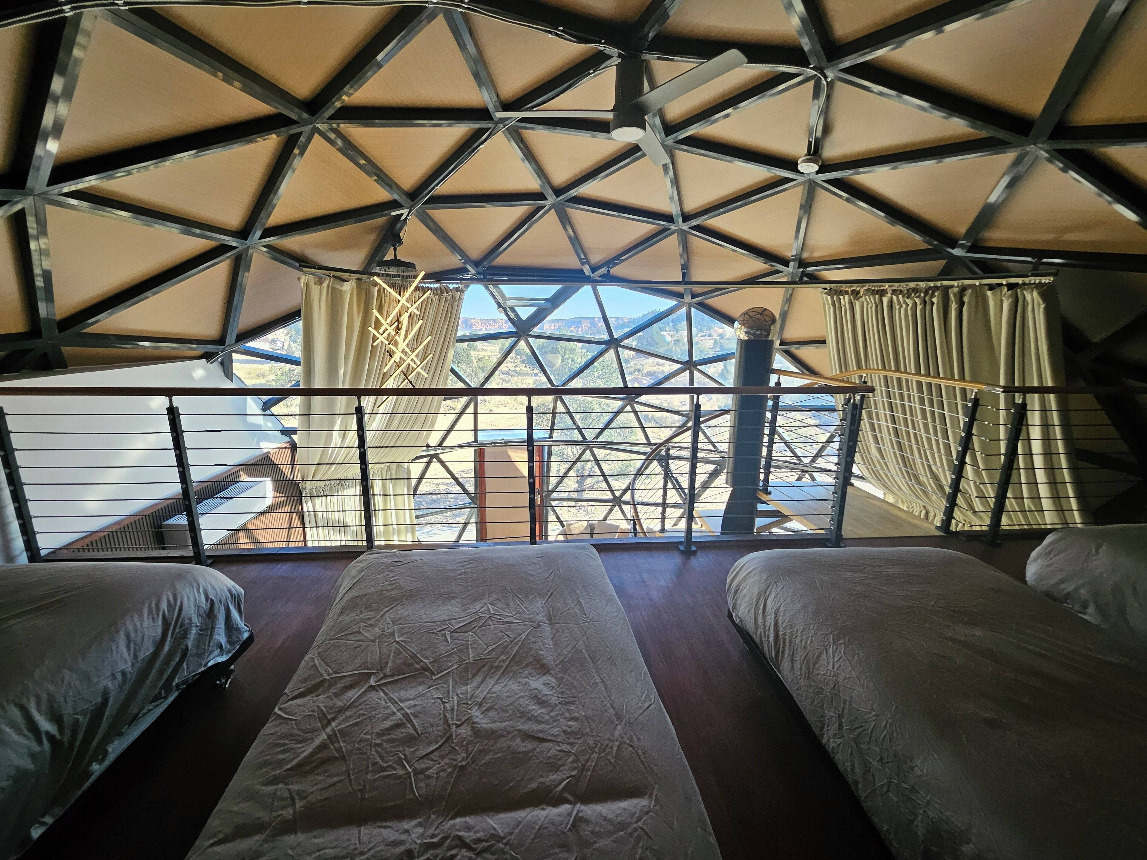 A room with a high ceiling and a view of a mountainous landscape. There are two beds with a large window in the center.