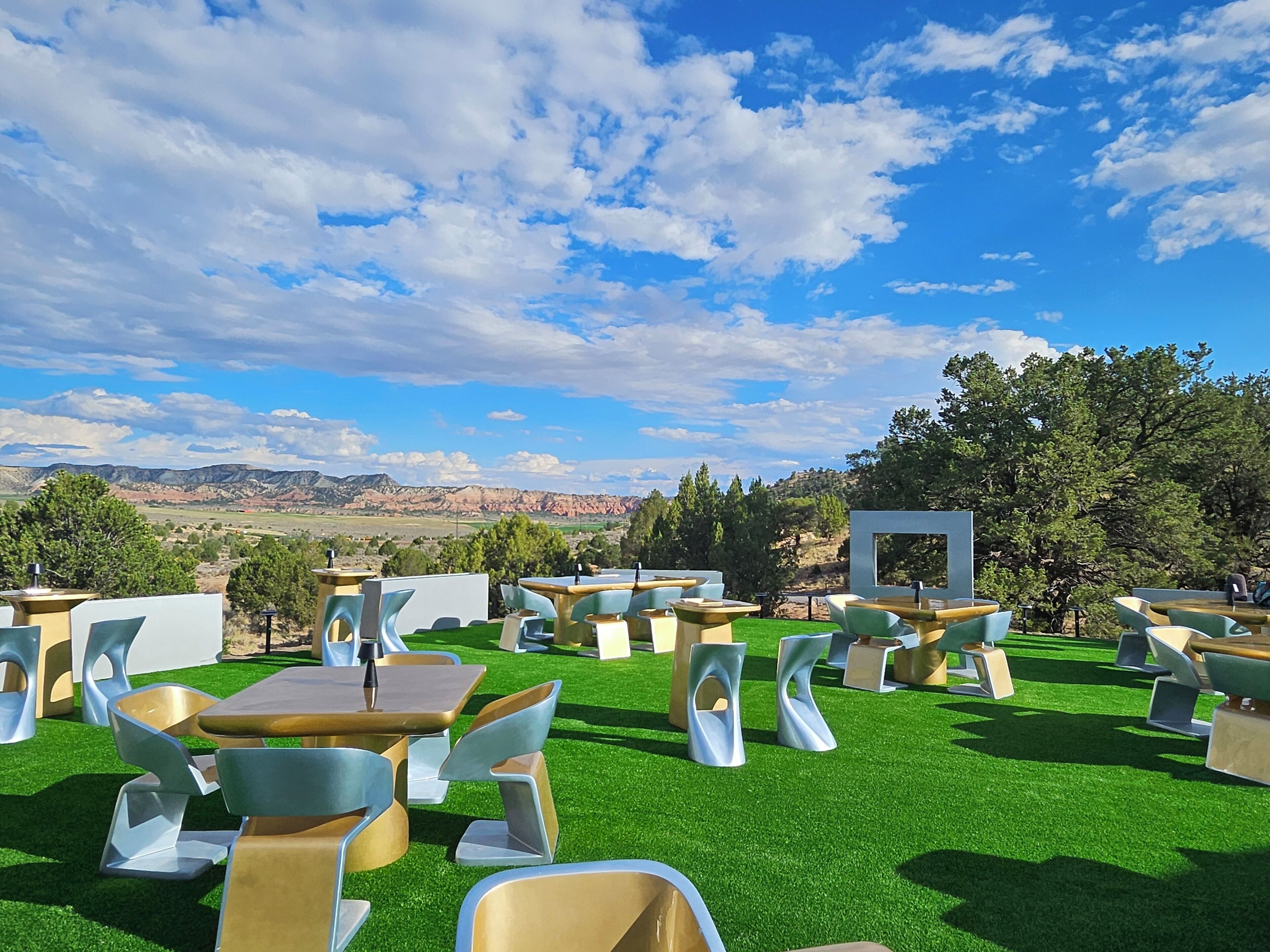 An outdoor seating area with tables and chairs, a view of mountains, and a clear sky.