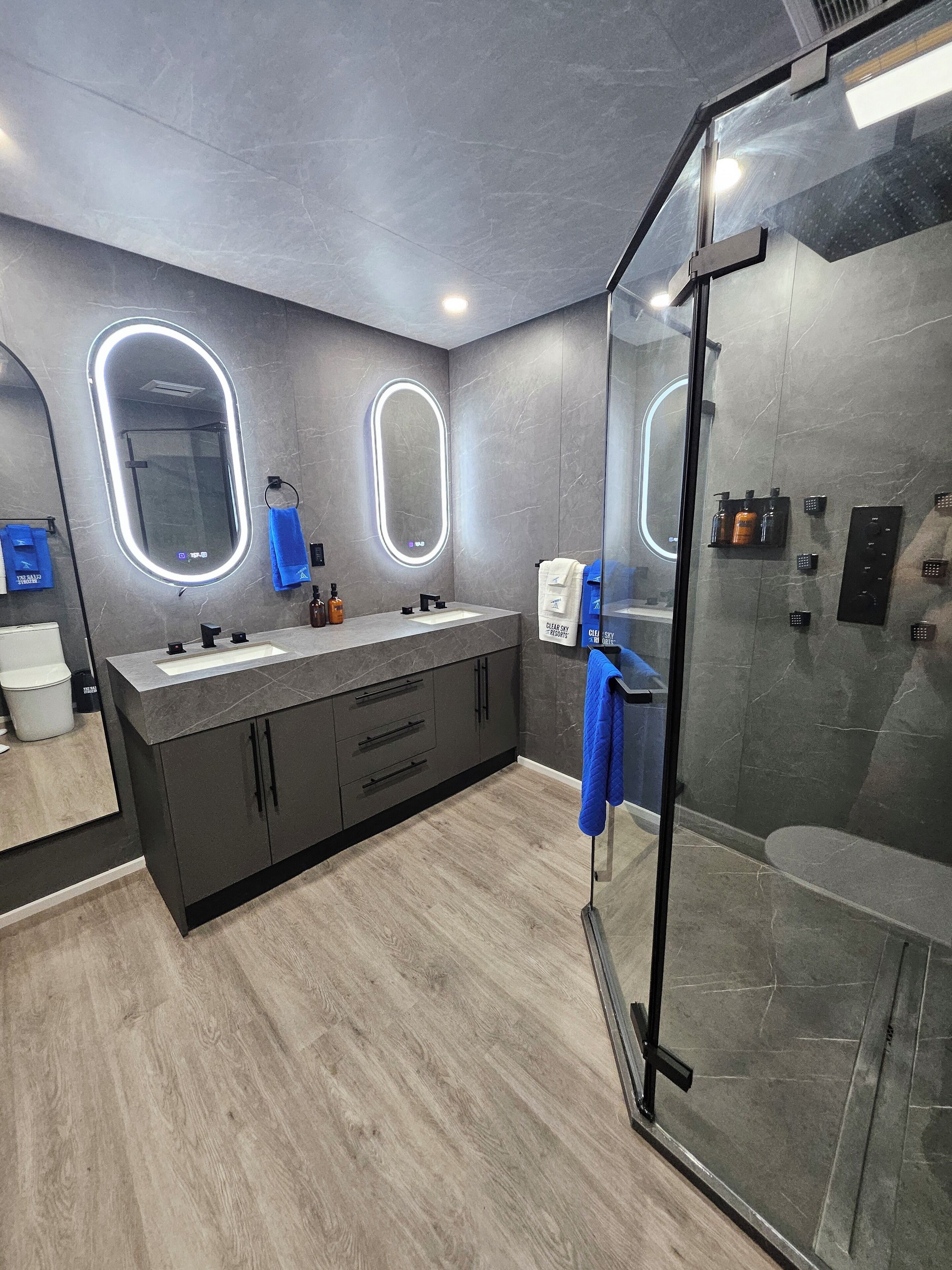 A modern bathroom with two sinks, a glass shower enclosure, and a large mirror with built-in lighting.