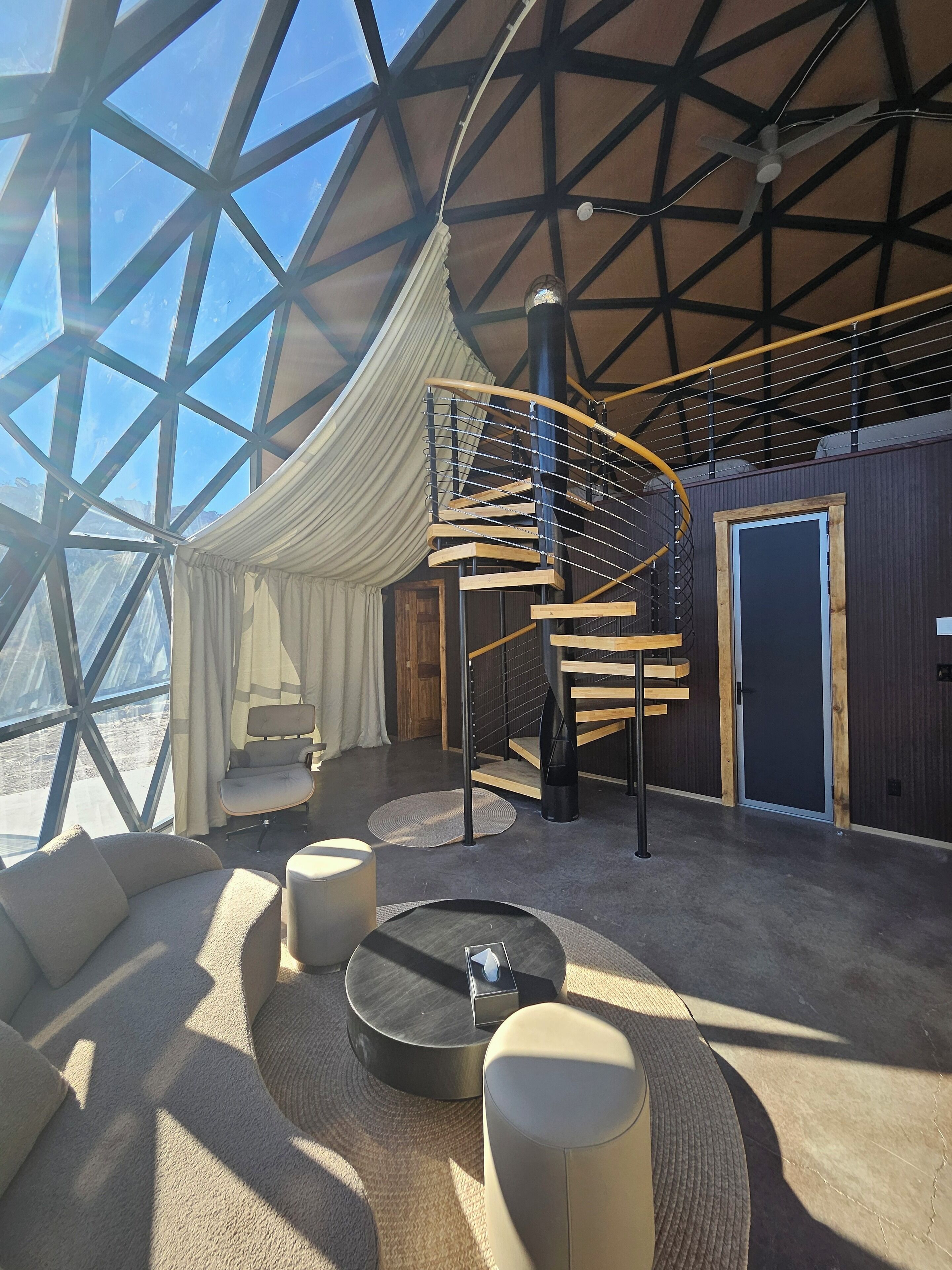 A spacious room with a large glass ceiling, a spiral staircase, and a cozy seating area with a sofa and ottoman.