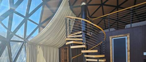 A spacious room with a large glass ceiling, a spiral staircase, and a cozy seating area with a sofa and ottoman.