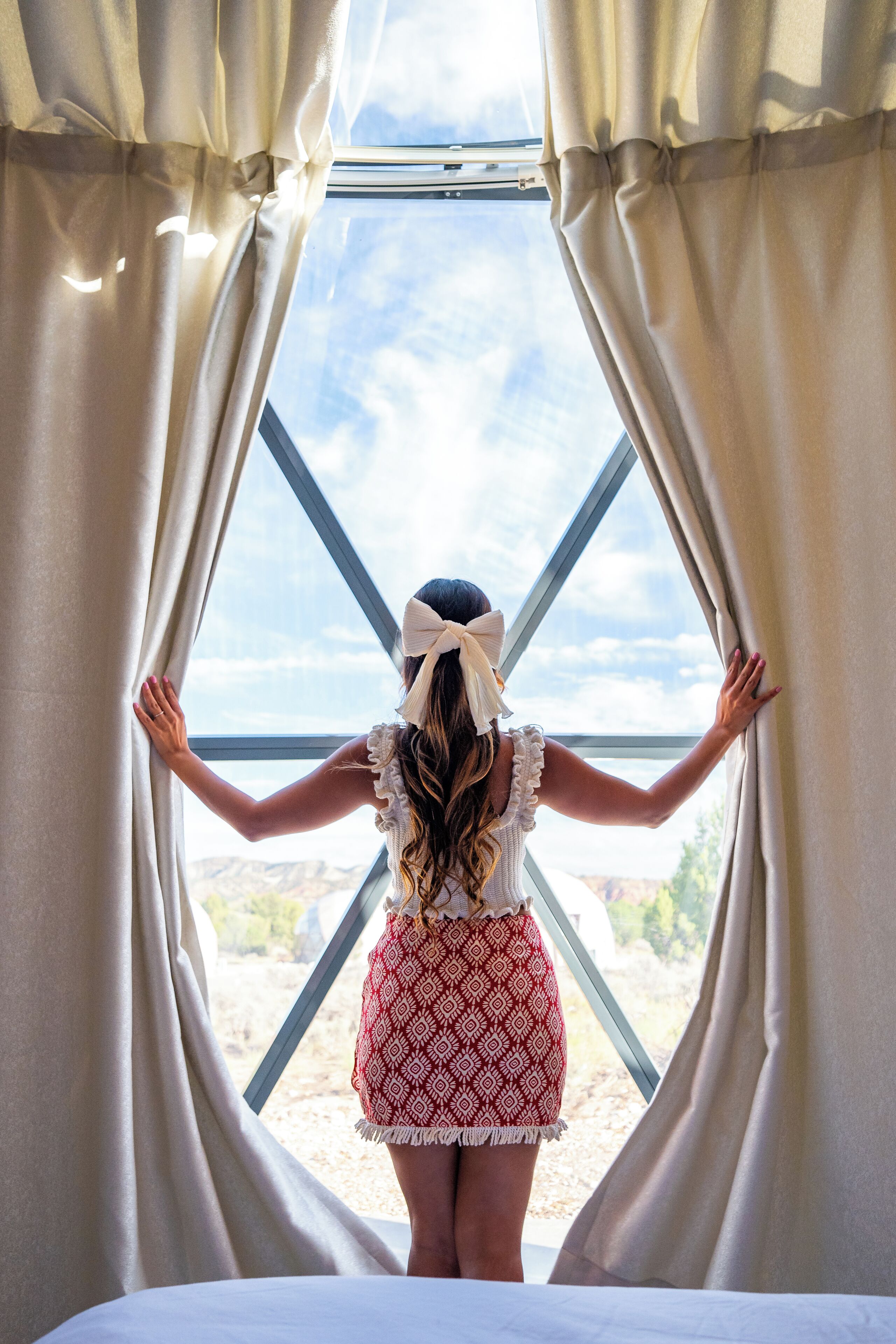 A person standing at a window with a view of a mountainous landscape.