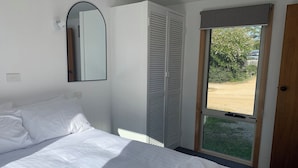 Habitación de hotel con cama, armario, espejo y ventana con vistas a zonas verdes.