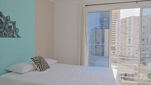 Un dormitorio con cama, ventana con vista a edificios y un adorno en la pared.
