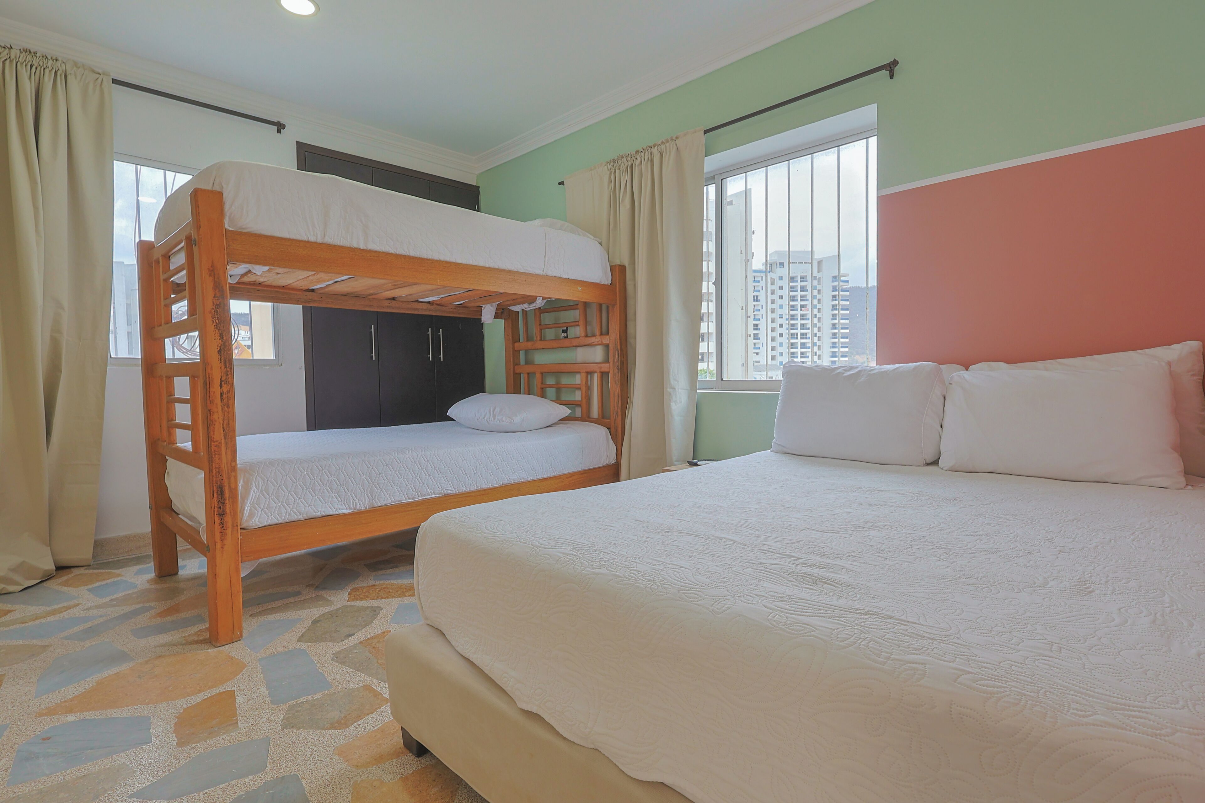 Una habitación con literas, una cama individual y una ventana con vistas a edificios.