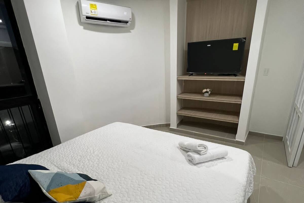 Una habitación de hotel moderna con una cama grande, un televisor de pantalla plana, un armario empotrado y un equipo de aire acondicionado.
