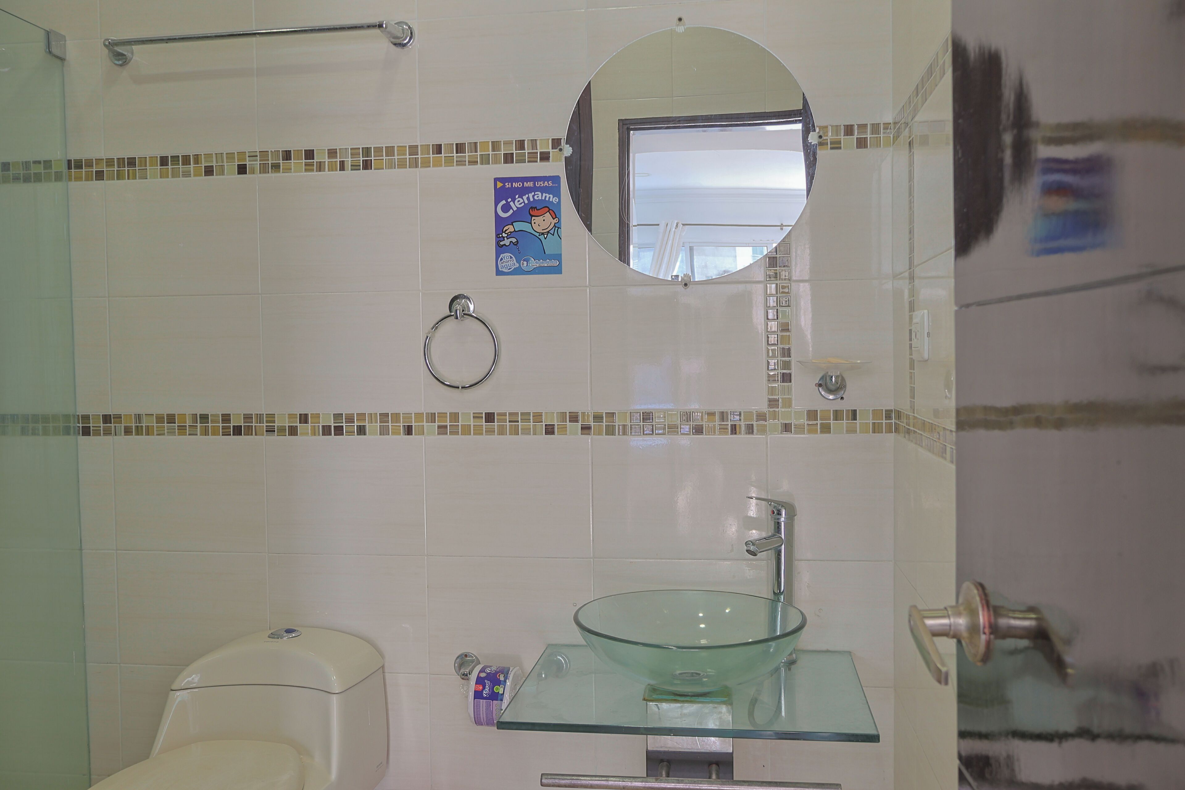 Ein Badezimmer mit einem Glaswaschbecken, einer Toilette, einem Handtuchhalter und einem Spiegel.