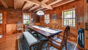 Interior de una cabaña de madera con una gran mesa de comedor, sillas, un banco y una lámpara de techo con vitrales.
