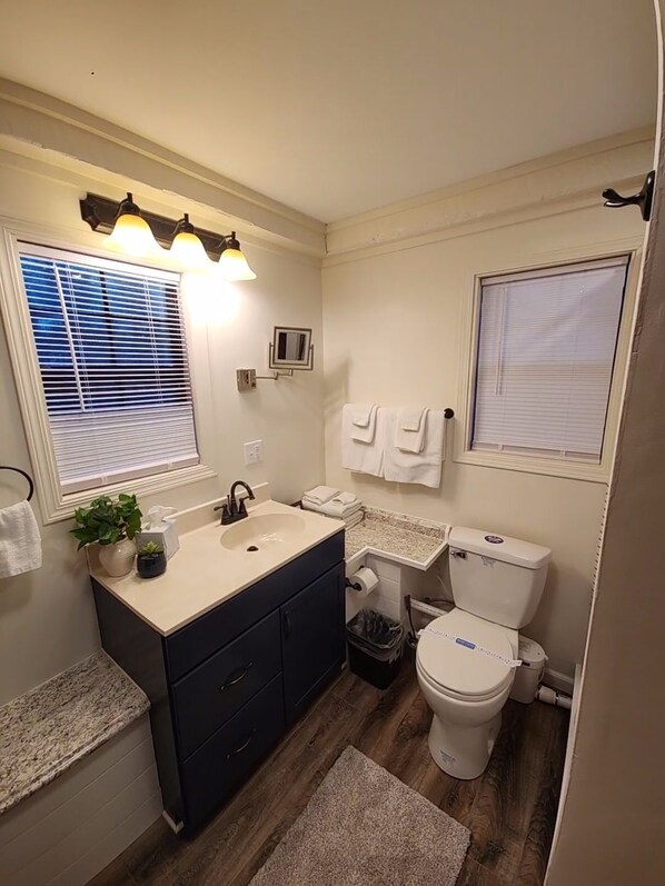Un baño con lavabo, espejo, toallero, inodoro y persianas.