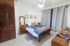 Quarto com cama, guarda-roupa de madeira, mesa de cabeceira e escrivaninha com cadeira.