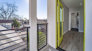 Un balcó amb barana metàl·lica, una porta amb marc groc i vista al barri.