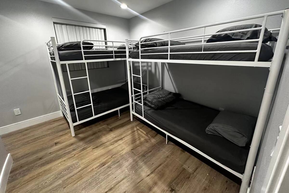 A room with bunk beds, wooden flooring, and a window with blinds.