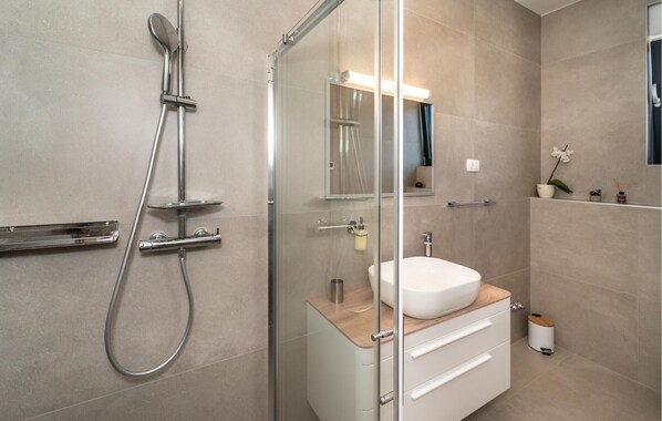 A modern bathroom with a glass shower enclosure, a white sink, and a wooden vanity. - Nice home in Posedarje with sauna (Posedarje)