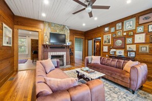 A cozy living room with wooden walls, a stone fireplace, a large flat-screen TV, and a collection of framed pictures.