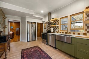 A modern kitchen with stainless steel appliances, green cabinets, and a large window with a checkered backsplash.