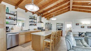 A spacious kitchen with wooden beams, a central island, bar stools, and a dining area with a sofa. - Beachfront Alligator Point Retreat: Steps to Sand! (Alligator Point)