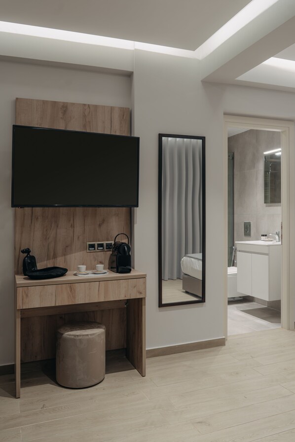 Una moderna camera d'albergo con una scrivania in legno, una TV a schermo piatto, un ampio specchio e un bagno separato.