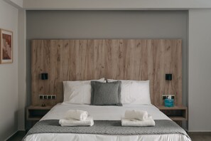 Habitación de hotel con cabecera de madera, ropa de cama blanca, dos mesitas de noche con lámparas y un cuadro en la pared.