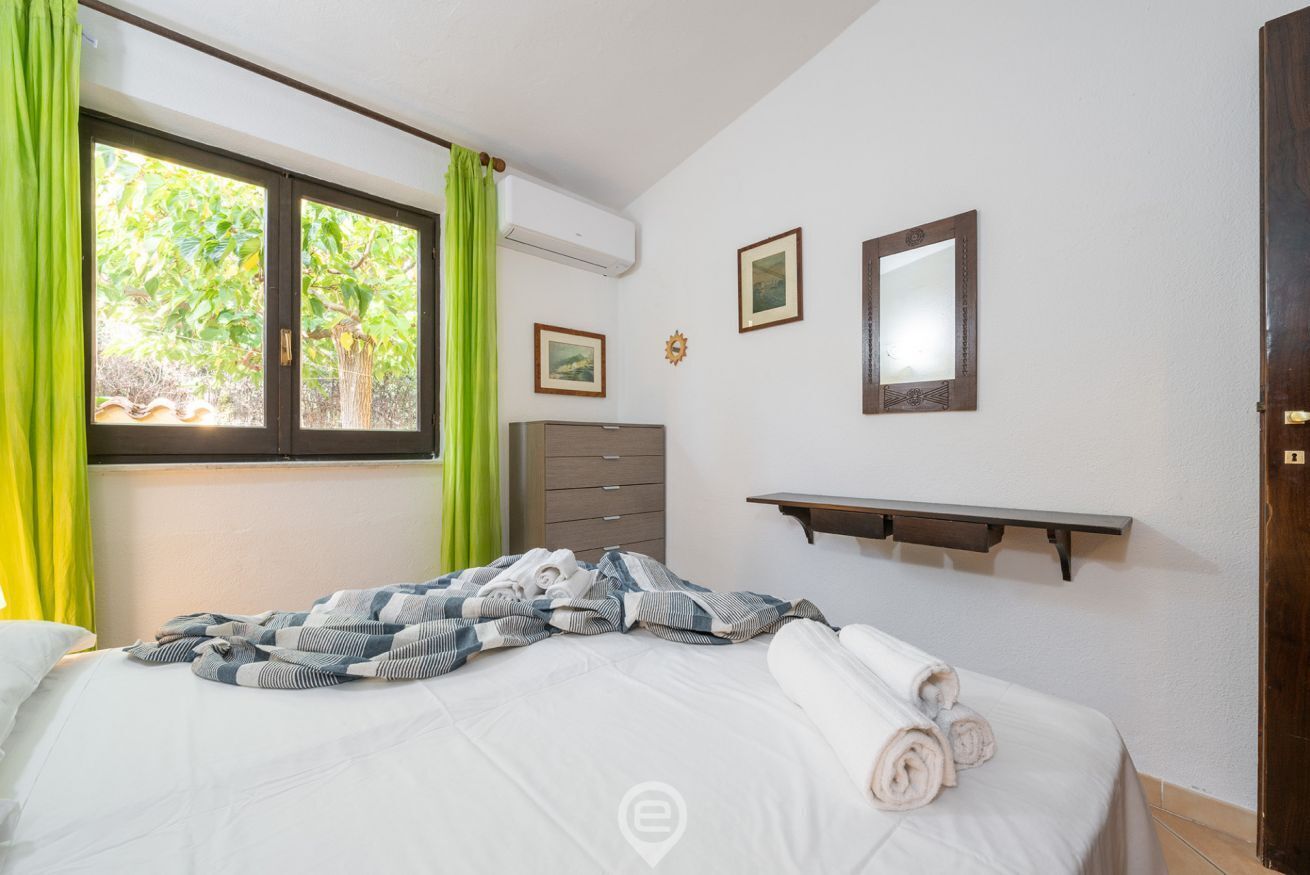 Een slaapkamer met een bed, een raam met gordijnen, een dressoir en een wandplank.