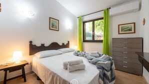 Een slaapkamer met een bed, nachtkastje, kaptafel en een raam met gordijnen.