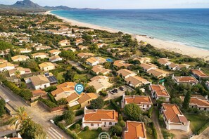 An aerial view of a coastal residential area with houses, a beach, and a clear sky. - Casa Anna - Monte Nai (Costa Rei)