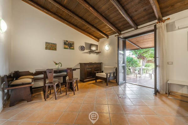 A spacious room with a wooden ceiling, tiled floor, a dining area with a table and chairs, a sofa, a cabinet, and a television. - Casa Anna - Monte Nai (Costa Rei)
