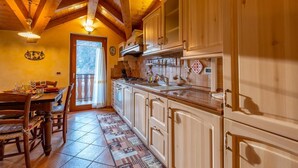 Een gezellige keuken met houten kastjes, een eethoek met een tafel gedekt voor vier personen, en uitzicht op de omgeving door een deur.